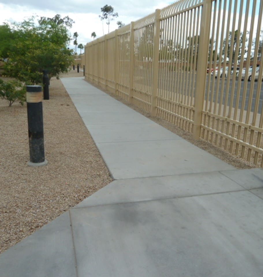 A sidewalk next to a fence.