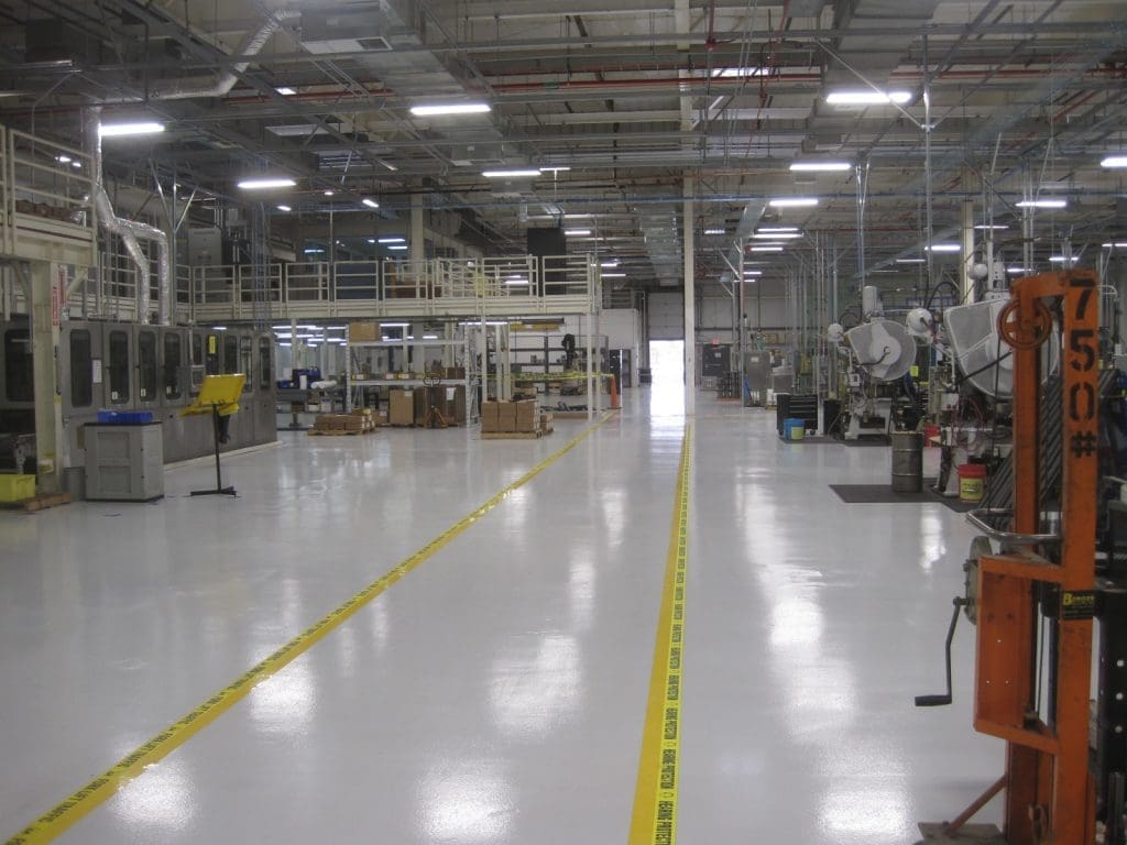 A clean, spacious factory floor with machinery, equipment, and boxes; yellow safety lines mark walkways through the industrial space.