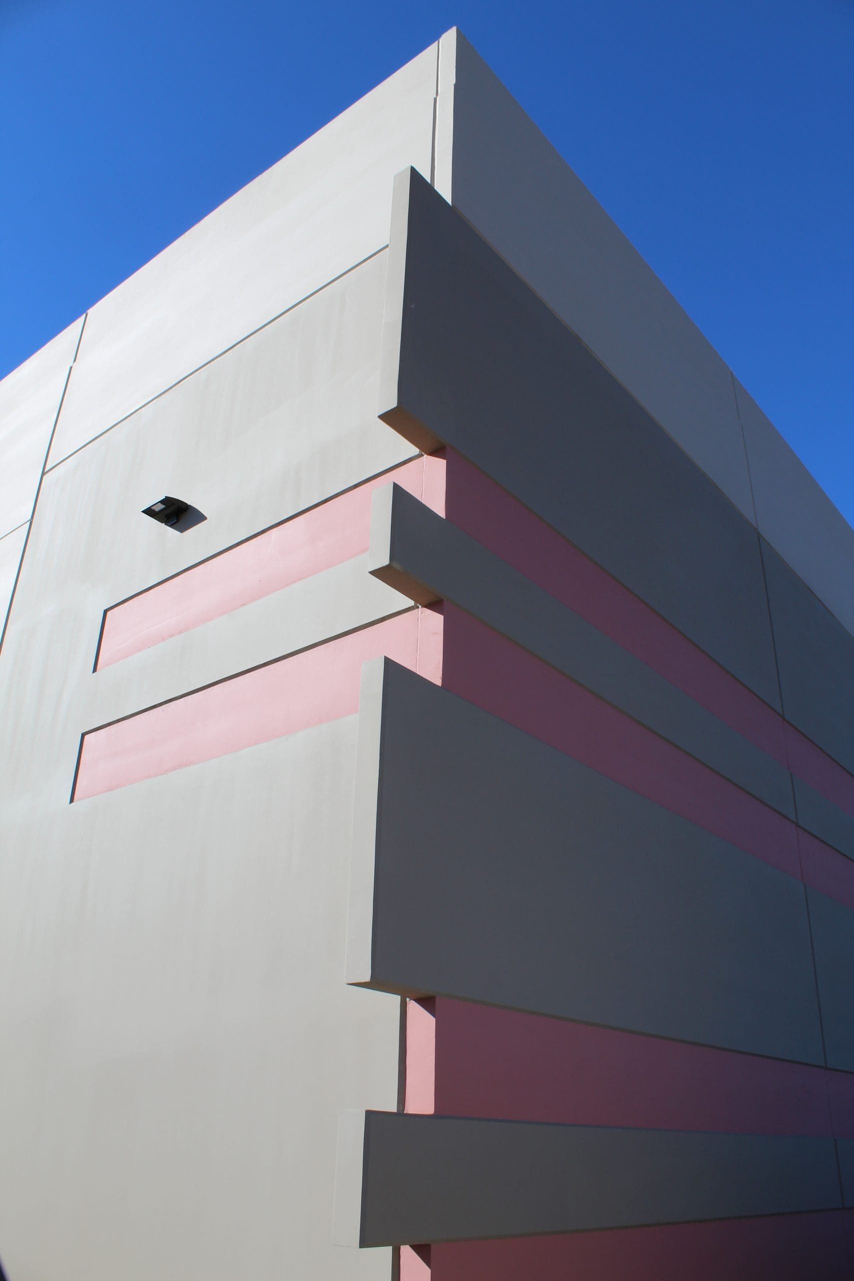 A geometric building corner with beige and pink panels, sharp edges, and a blue sky in the background.