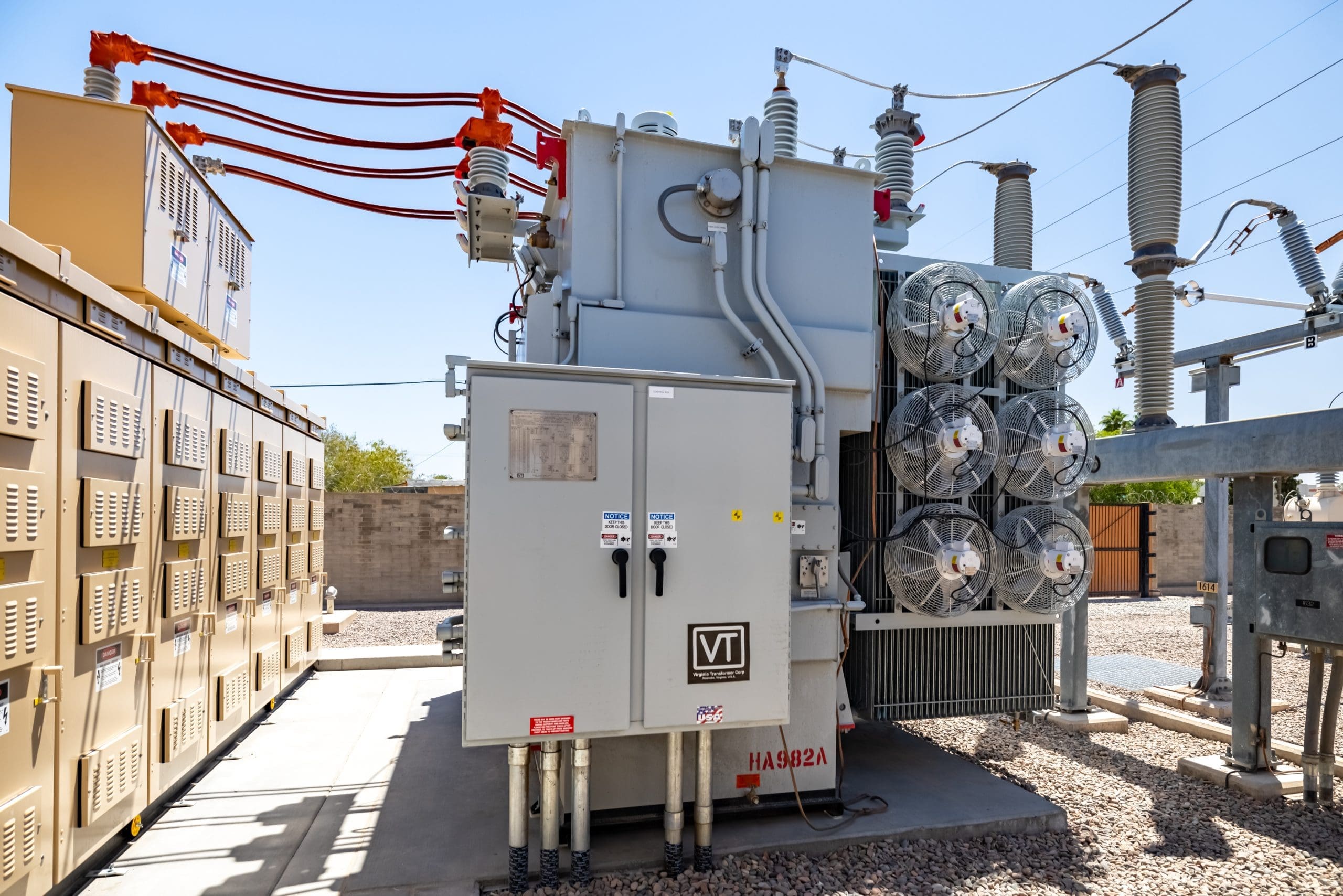 A large electrical transformer with cooling fans and insulated power cables at an outdoor substation.