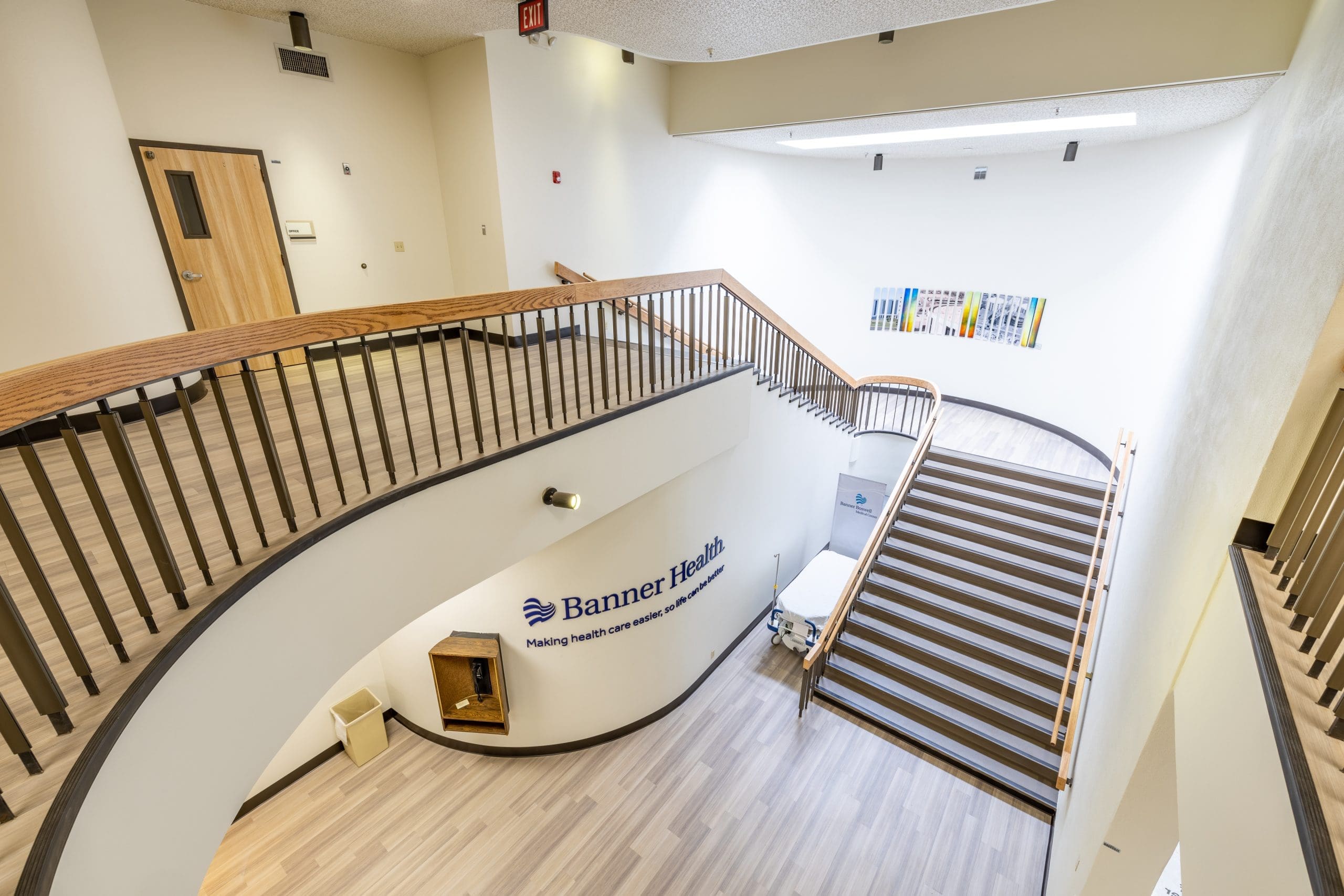 Wide view of a modern indoor staircase and landing area at Banner Health, with wooden railings, light flooring, and a wall-mounted artwork.