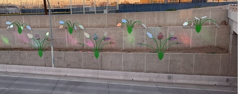 Concrete retaining wall along a road features multiple large, stylized flower murals painted in green, white, pink, and purple.