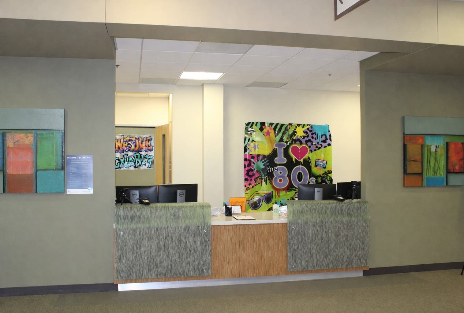 A front desk with two computer stations, modern abstract art on the walls, and a colorful "I love the 80s" mural in the background.