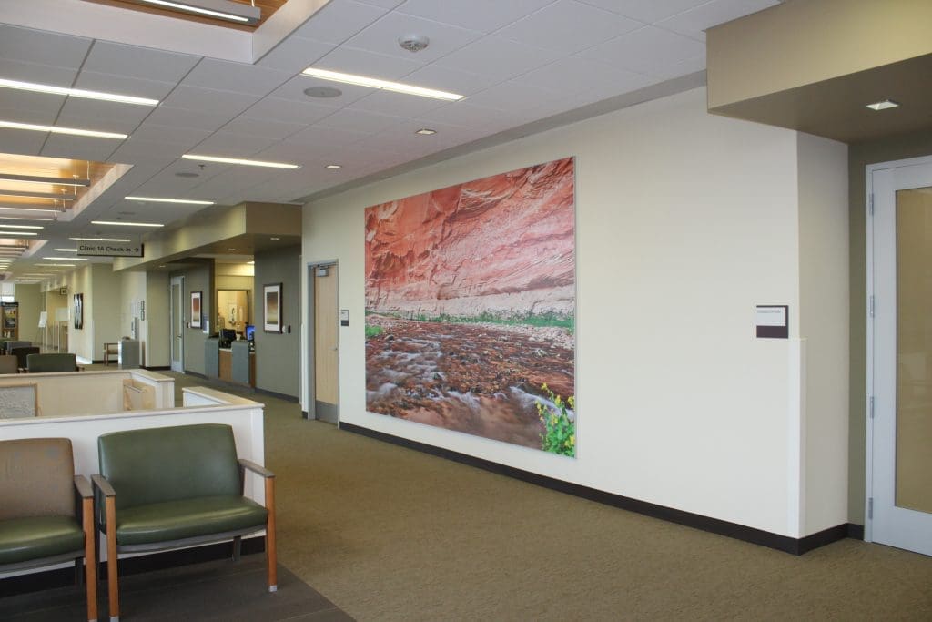 A large photograph of a red rock landscape hangs on a cream-colored wall in a modern office waiting area with chairs and overhead lighting.